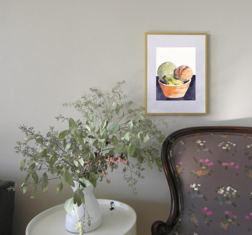 In situ view of framed painting of two cantaloupes in a wooden bowl.