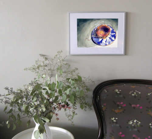 Small colourful watercolour painting framed on a wall above an armchair and a sidetable with a vase and bouquet.