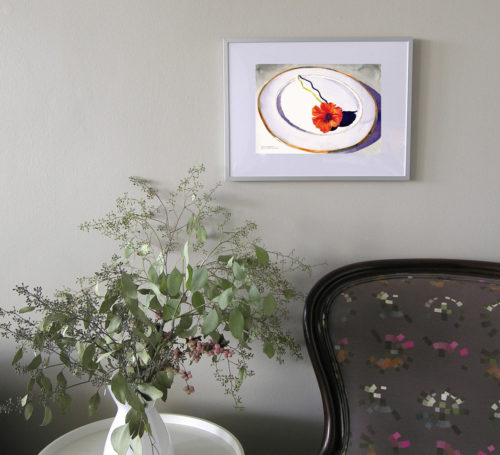 Scene of a small watercolour painting of a single orange nasturium blossom on a white gold-rimmed china plate