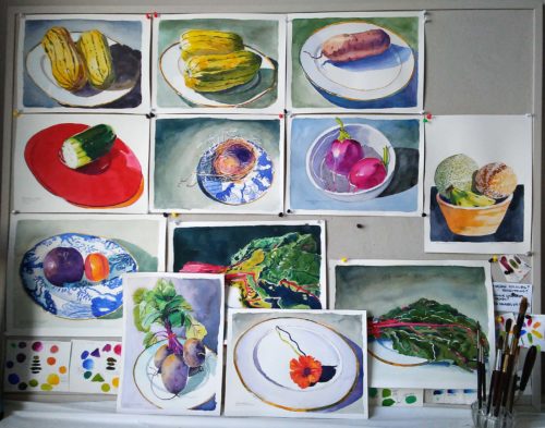 View of a studio bulleting board filled with small watercolour paintings of vegetables on china plates.