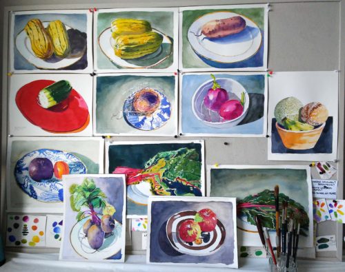 View of small watercolour paintings of vegetables on china plates on a bulletin board
